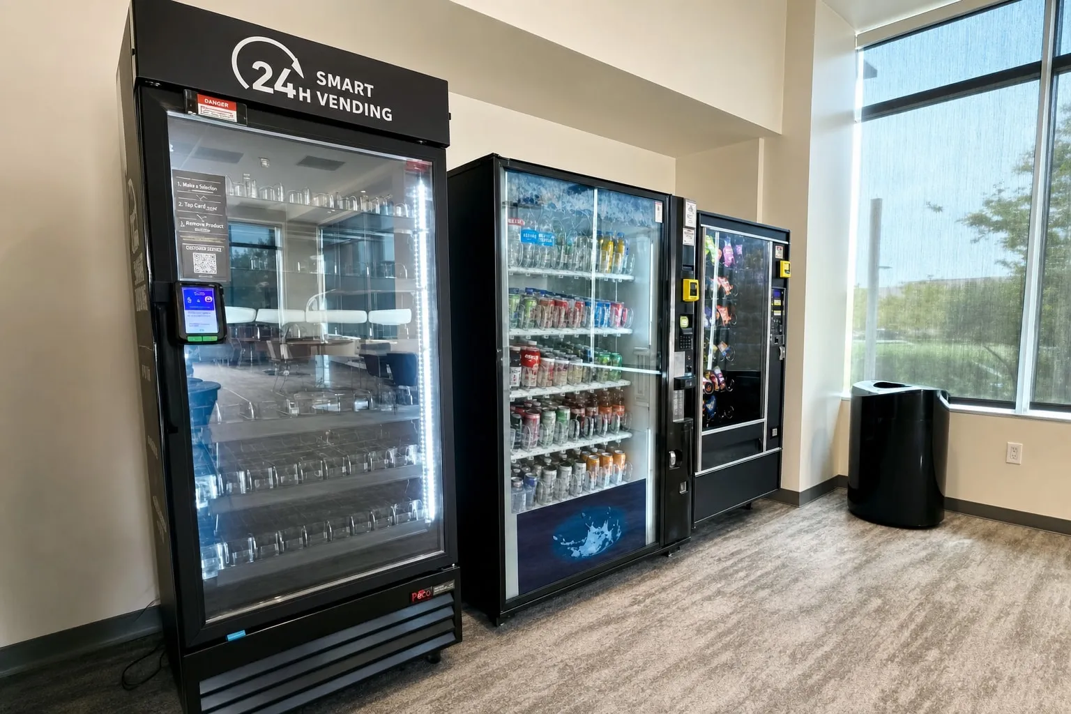 Smart cooler, cold drink vending machine and snack vending machine installed together beside office windows, all with cashless tap-to-pay readers